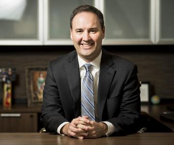 Man with hands folded sitting at a desk.