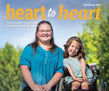 Preteen girl kneels next to younger girl who is in a wheelchair.