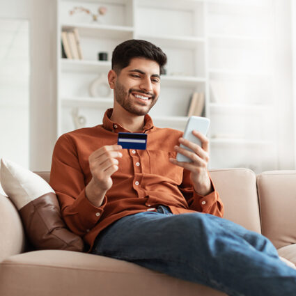 Man paying bill from sofa with credit card and cell phone in hand