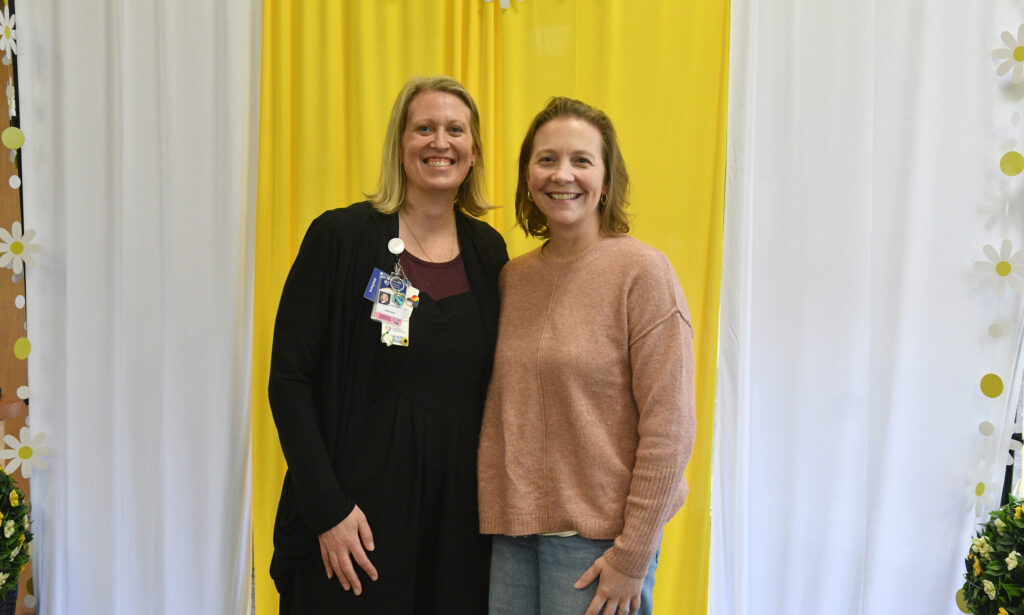 Woman in copper colored sweater stands next to a woman in a black sweater. 