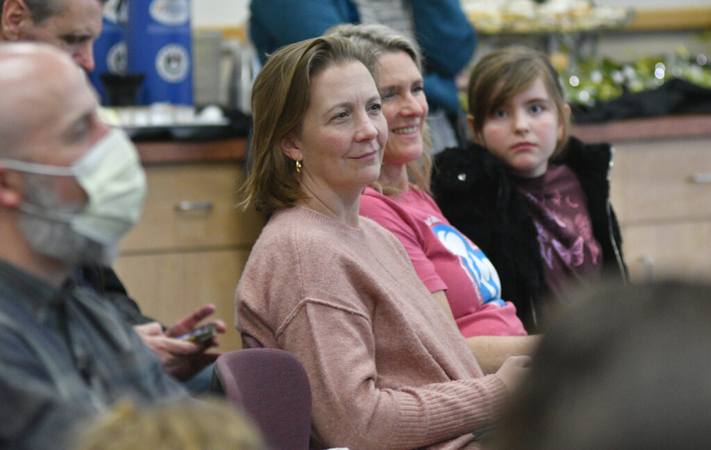Woman in copper colored sweater wits next to a woman in a pink tee shirt and a girl in a black jacket. 