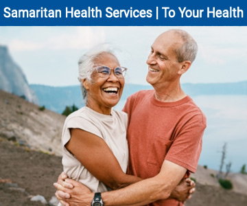 A couple smiling as they embrace in front of Crater Lake. August - To Your Health banner image.
