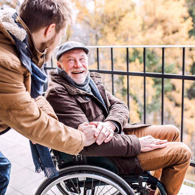 Older adult in a wheelchair smiling at a family member.