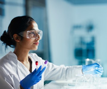 Person in lab coat, safety glasses, gloves, and glassware.