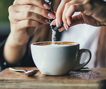 A woman's hands putting sweetener into her coffee.