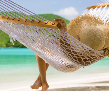 A person laying in a hammock on the beach, wearing a straw hat.