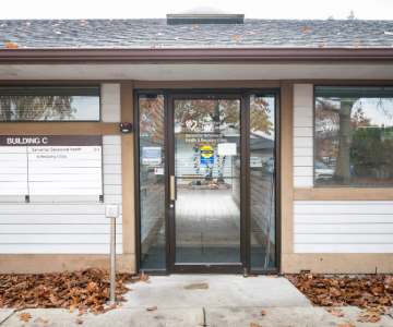 The front of the clinic building. The building is white and tan with a glass door.