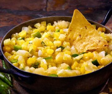 Pineapple salsa with chunks of green bell pepper in a cast iron bowl with a tortilla chip.