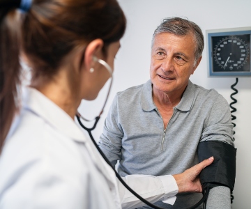 Female doctor taking middle-aged man's blood pressure in a doctor's office.