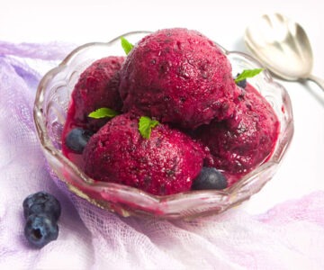 Four scoops of blueberry sorbet in a clear glass bowl.