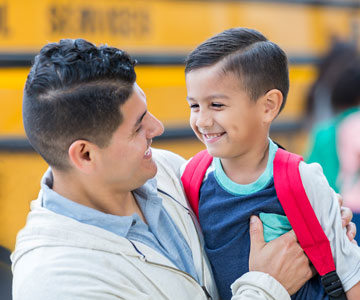 Dad smiling at his young child and hugging him before getting on the school bus.