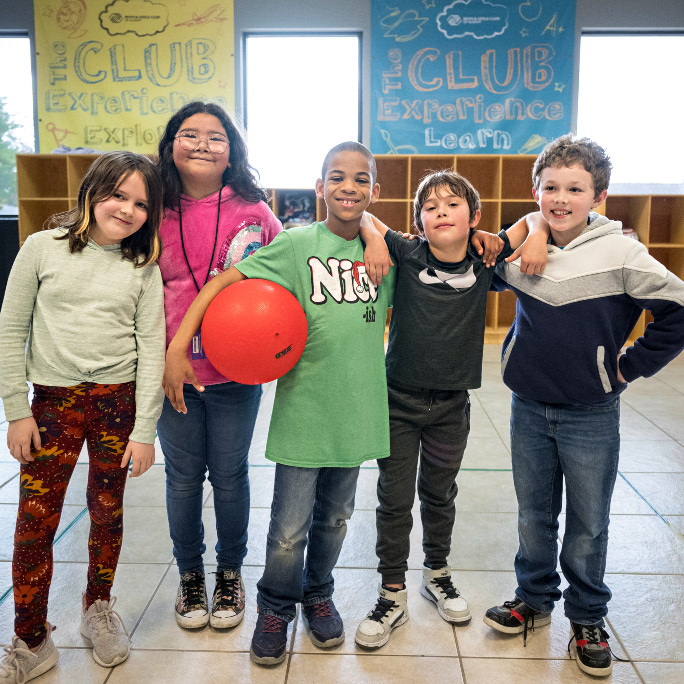 Row of standing children with ball indoors.