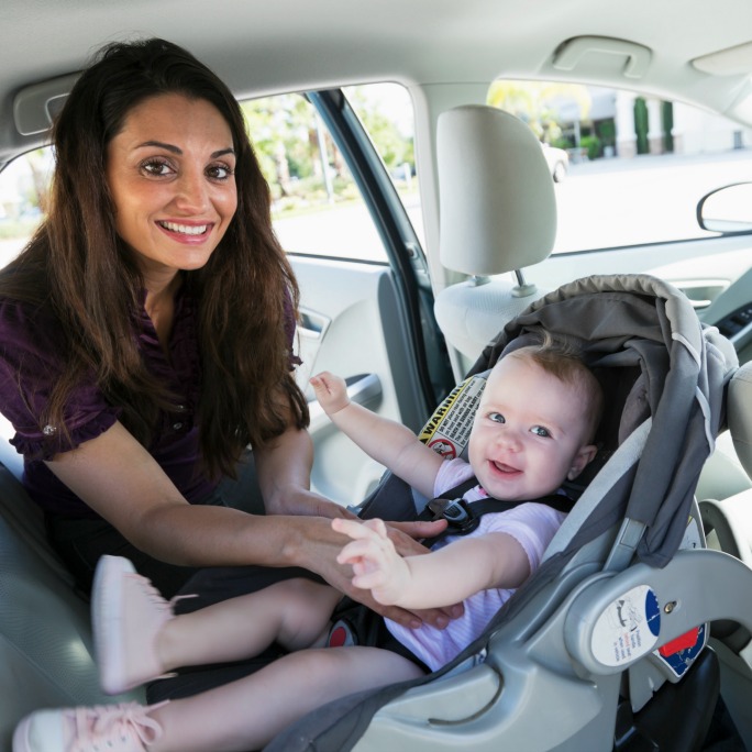 Parent strapping baby in car seat