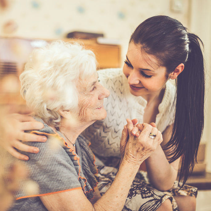 Frail older woman holding hands with her caregiver.