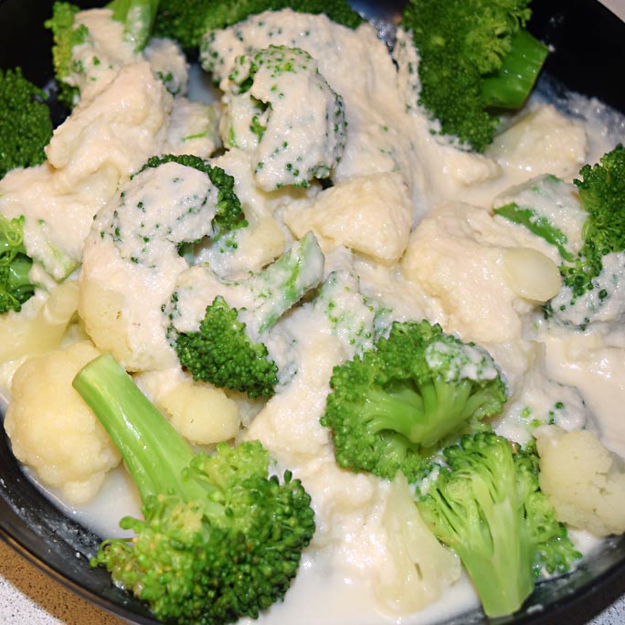 Bowl of broccoli covered in cashew white sauce.