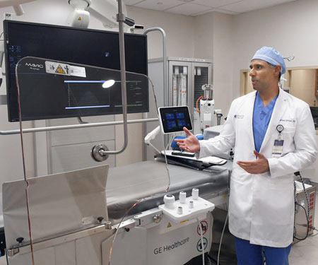 A man wearing a white lab coat shows a large screen and procedure table.