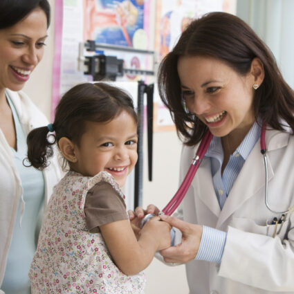 Toddler girl laughing while doctor examines her heartbeat.