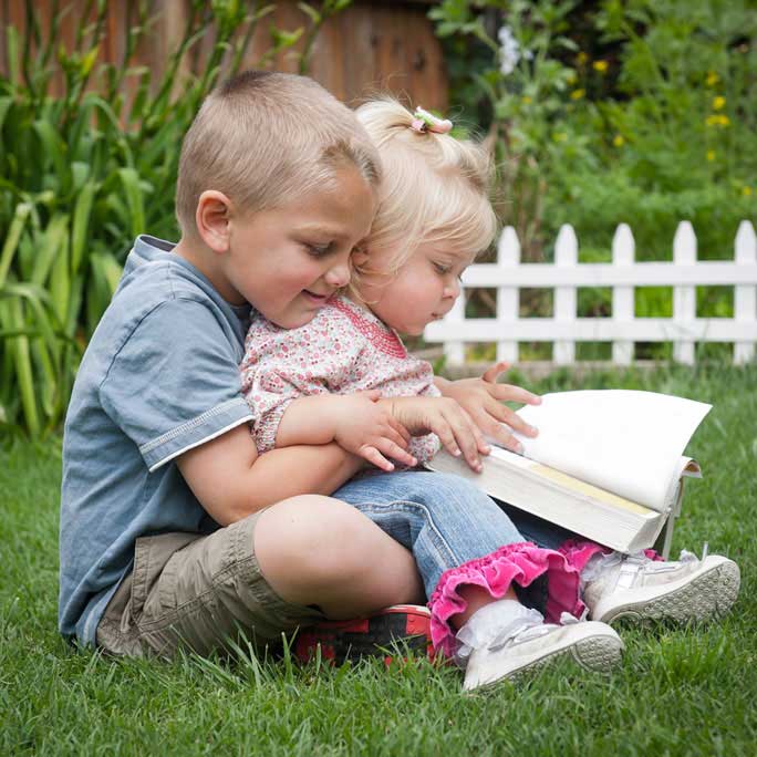 Little boy and little girl sitting on the grass reading a book