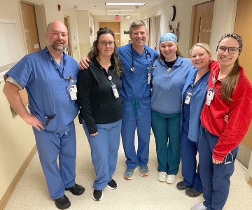 Six people stand in a hallway all wearing scrubs.