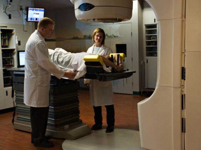 Clinicians move a patient under head of radiation unit.