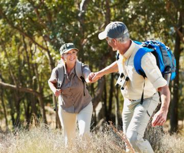 An older couple hiking through a grassy oak savannah.