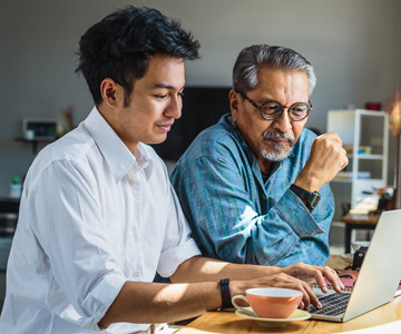 Younger man typing on computer while older man looks on