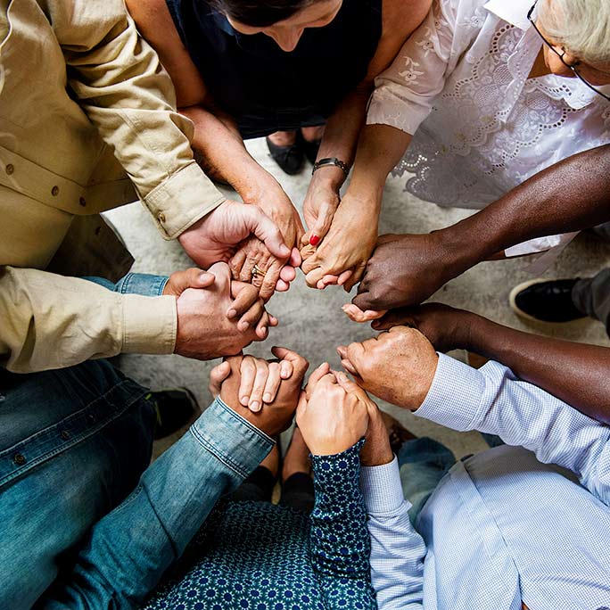 Close up of a diverse group of people holding hands that form a circle.