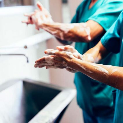 Two medical professionals scrub hands with soap in front of a sink