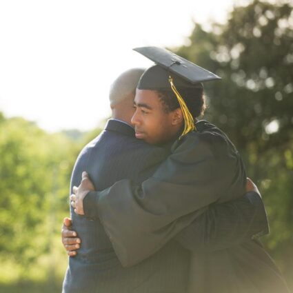 Black father and son hugging at graduation ceremony