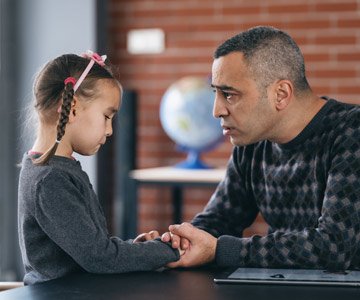A father talking to his sad young daughter with her hands in his.