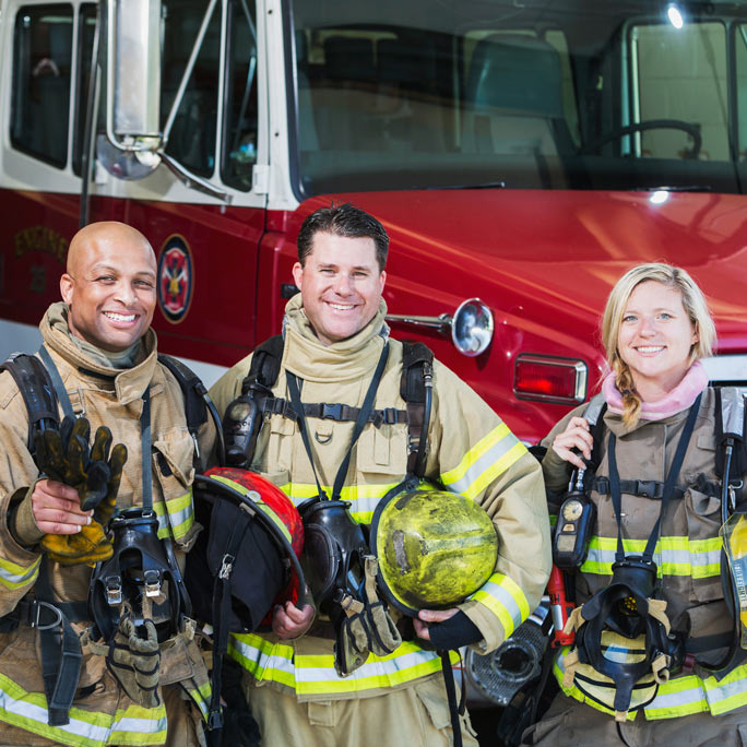 Smiling firefighters in front of red fire truck.