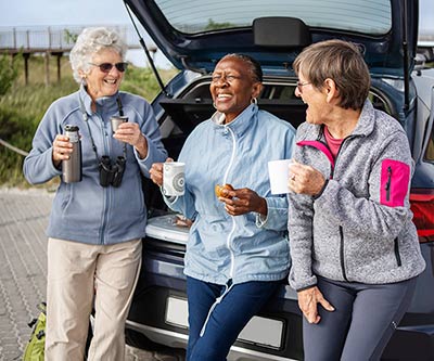 Three laughing women sitting on the tailgate of their car on a road trip together.