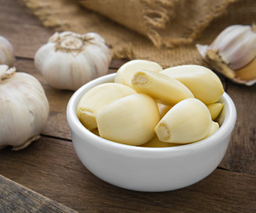 Bowl of peeled garlic surrounded by garlic cloves.