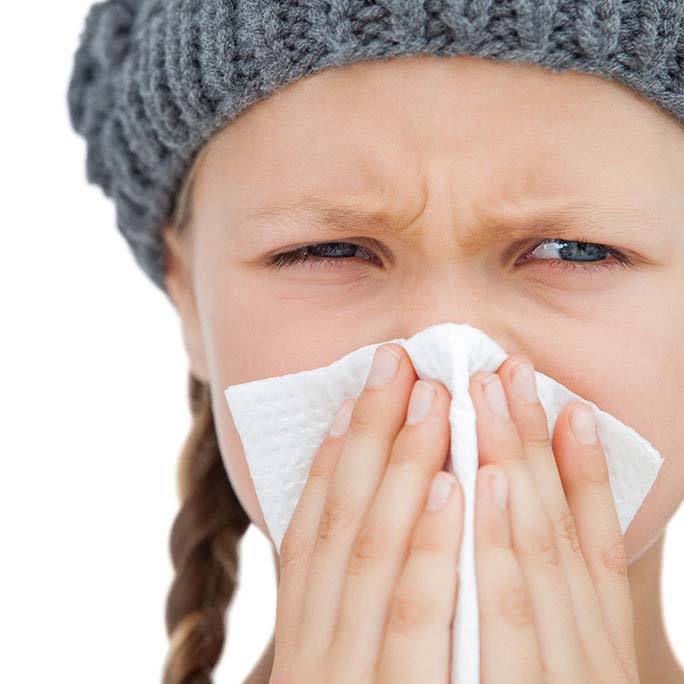 girl in hat who has the flu blows her knows with a white tissue