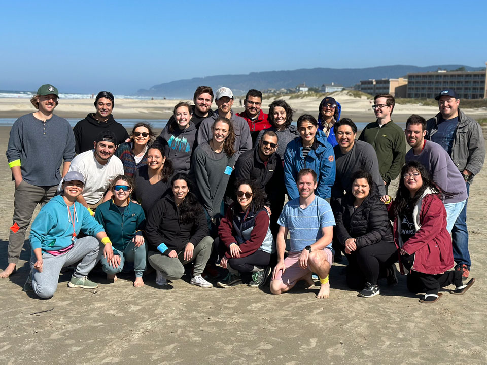 Men and women pose for a photo in sand on the beach at the Oregon Coast