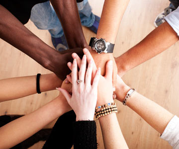 Several diverse hands piled on top of each other creating a circle with their arms