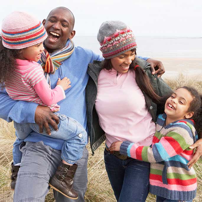 Black mother and father smiling with their two daughters on a beach walk