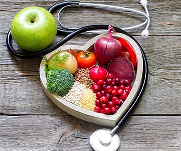 Fruit and veggies in a heart shaped dish surrounded by a stethescope