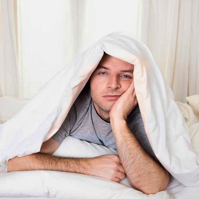 Man under covers not sleeping well and looking tired.