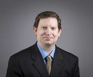 Man in black jacketwearing blue shirt and gold tie