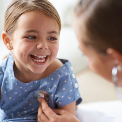 Female doctor listening to smiling little girl's heartbeat while providing health services