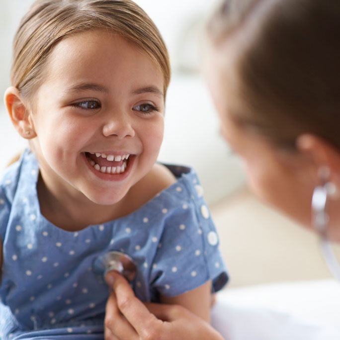 Female doctor listening to smiling little girl's heartbeat while providing health services