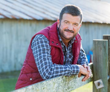 Man outdoors in red vest by fence