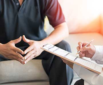 Close up of a man's hands showing stress as a health care provider goes through a check list on a clipboard.