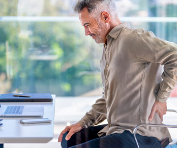 Man sitting and grabbing his lower back due to back pain.