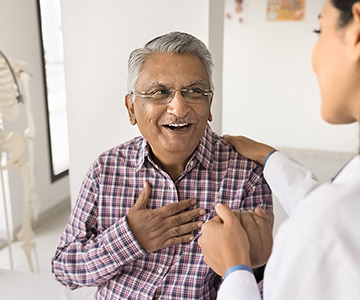 Young doctor holding hands and talking with senior patient with chest pain.