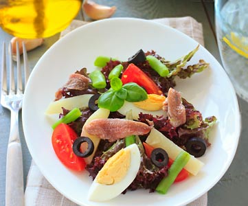 A bowl of fresh greens, hard boiled egg, olives, tomatoes, basil and grilled chicken.