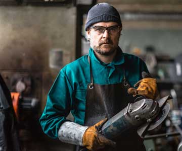 Person in leather gloves and apron holds grinding tool.