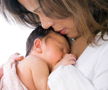 A mother's head bowed and snuggled close to her newborn baby.