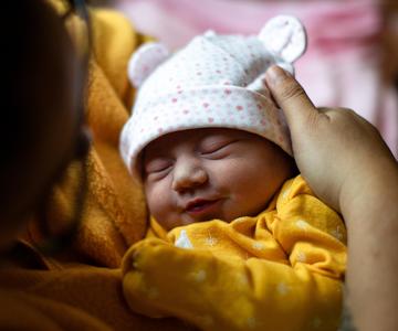 A smiling newborn baby being held.